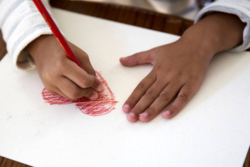 a child draws a heart on a peice of paper.