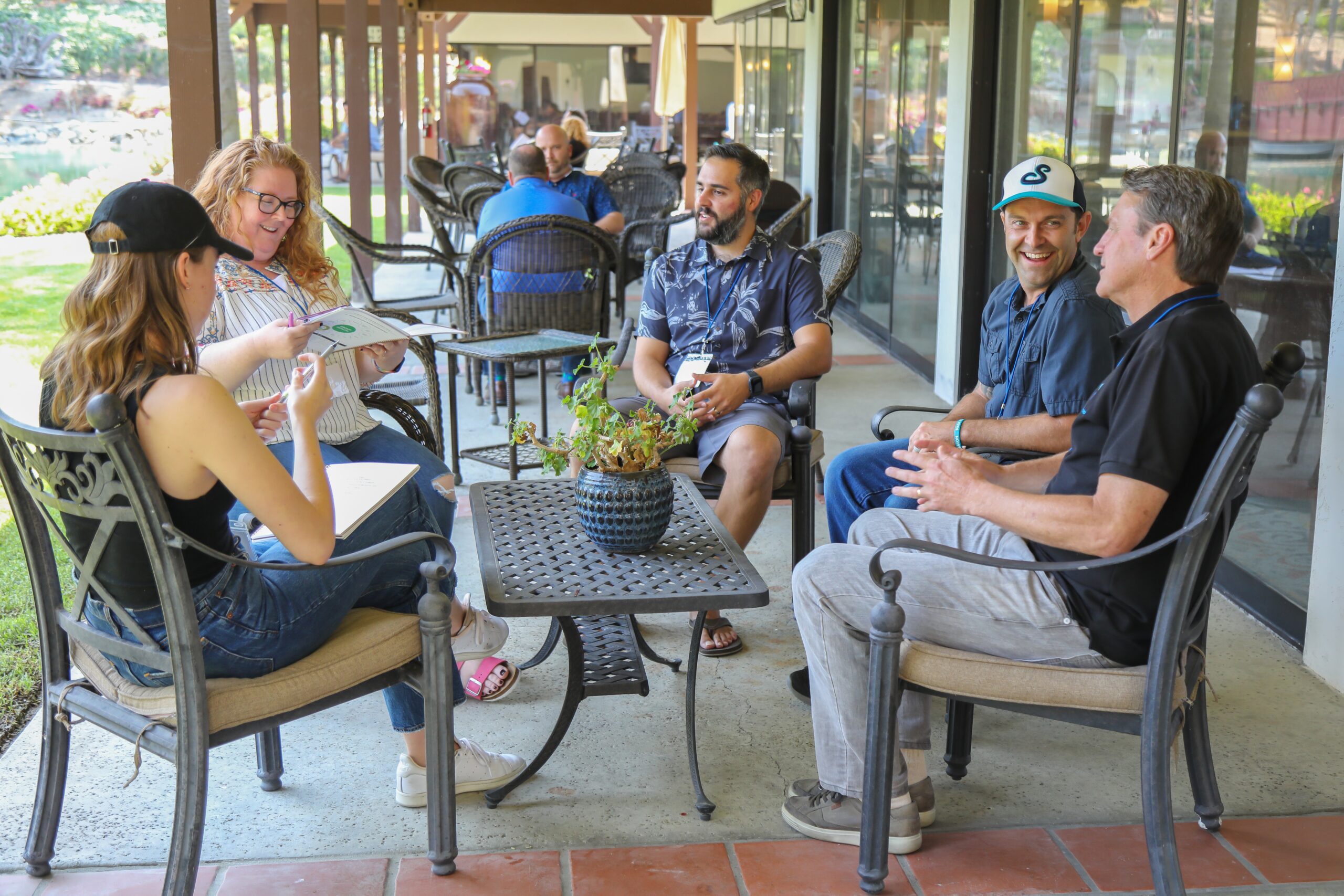 five middle aged white people of various genders sit around a patio table.