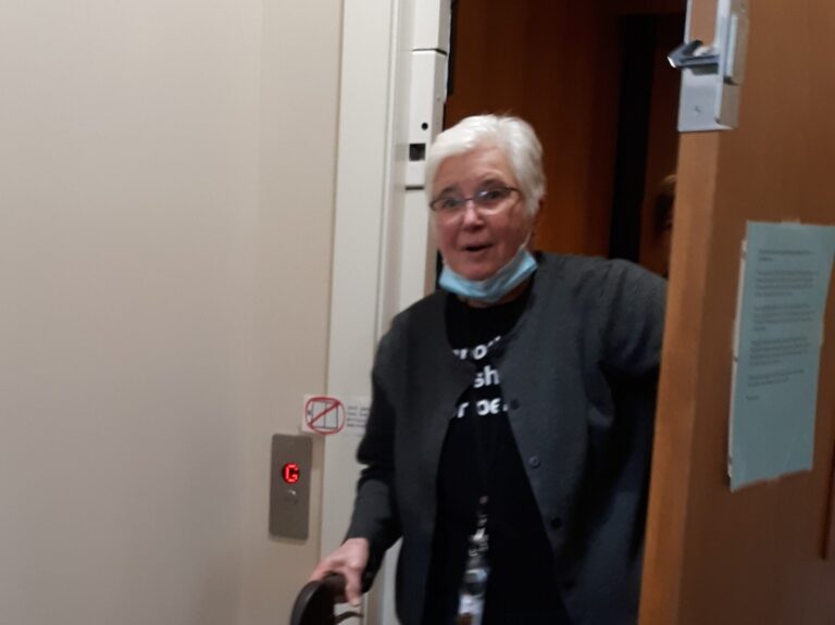 an elderly white woman using a walker emerges from a lift.