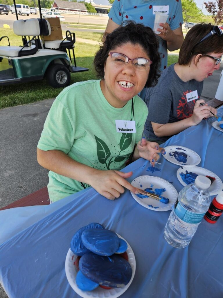 a dark-skinned female young adult with visible signs of intellectual disability paints a rock.