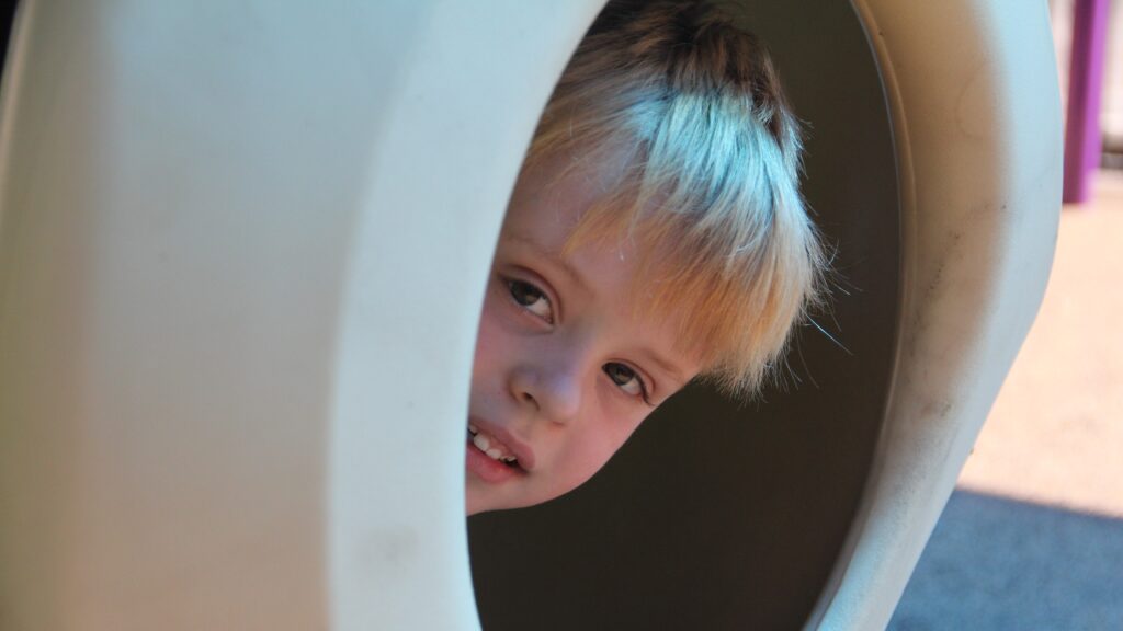 a small white child pokes his head out of an enclosure.