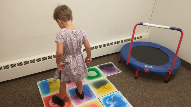 a young white child steps on a sensory floor mat.