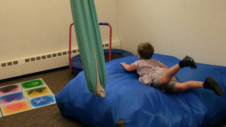 a child flops onto a large floor pillow in a sensory room.