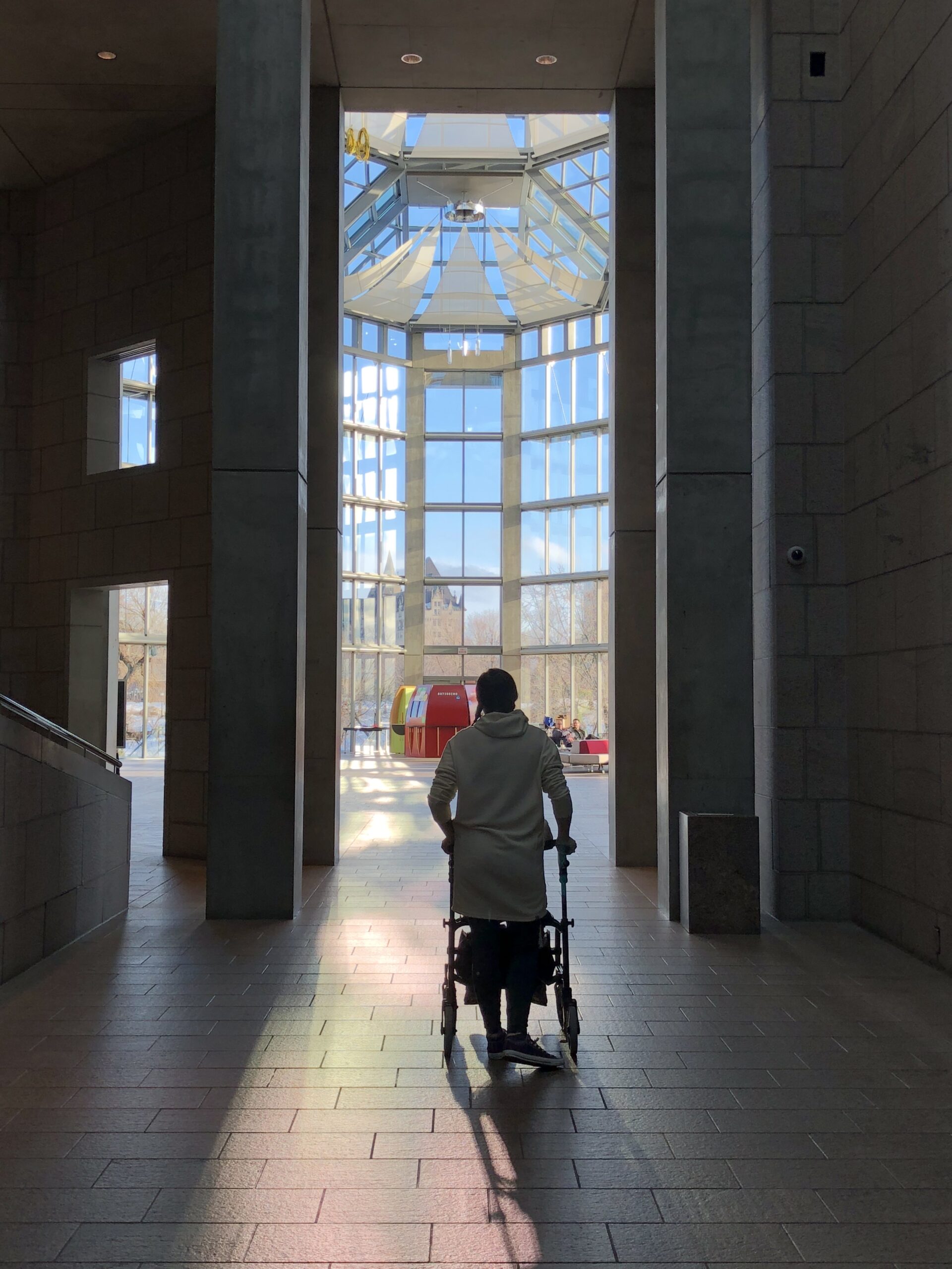 a woman using a walker stands in a doorway with light spilling over her.