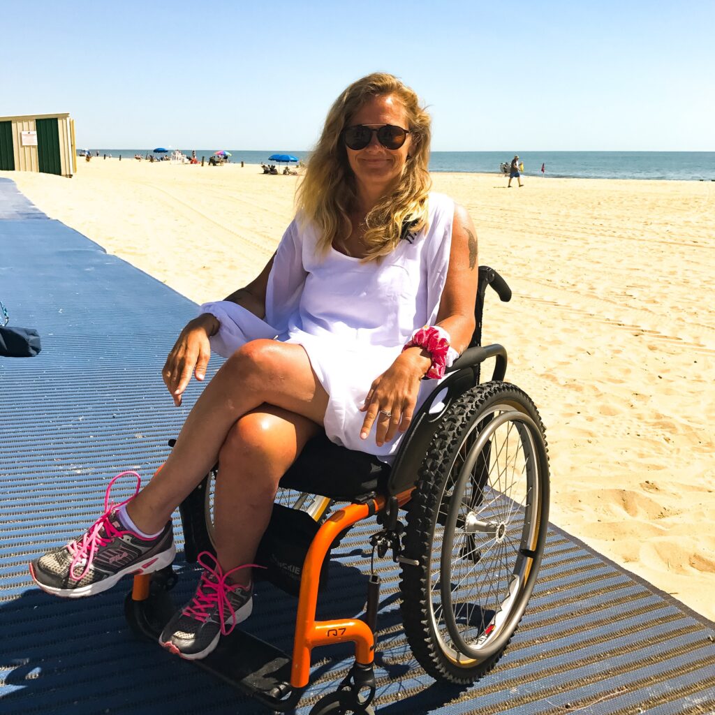 Shelly is a middle-aged white woman sitting in a wheelchair at the beach.