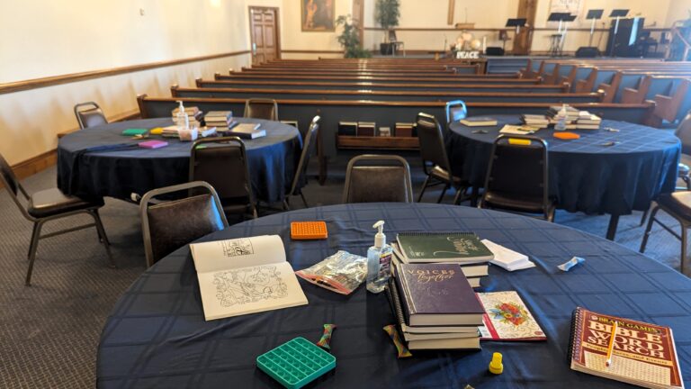 circle tables in the back of a worship area. On the tables are puzzles, fidget tools, and coloring books.