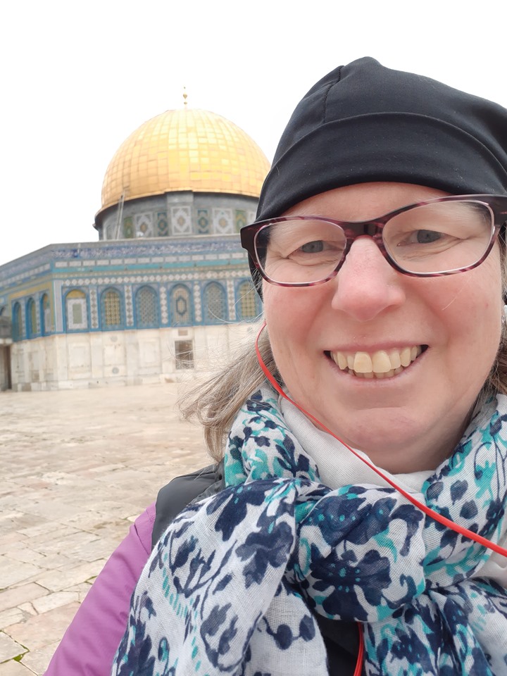 Michelle is a young adult white female wearing a hat and scarf and standing in front of a mosque.