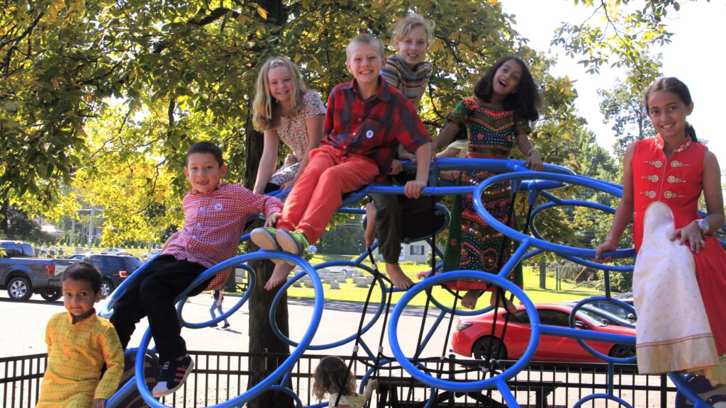 eight children of various ages, ethnicities, and genders smile jubilantly on a climbing structure.