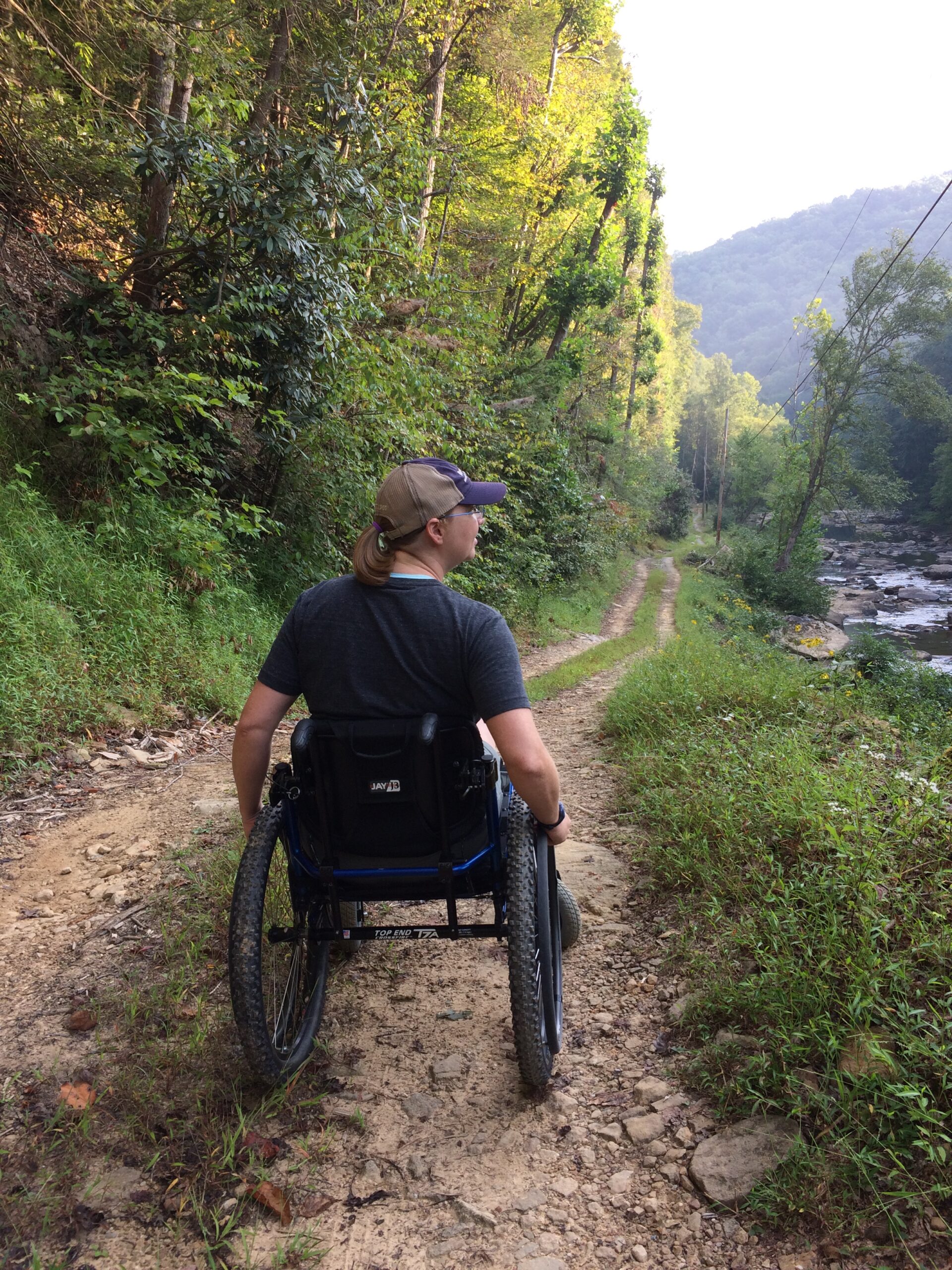 a woman in a wheelchair on a dirt path that cuts through a forest.