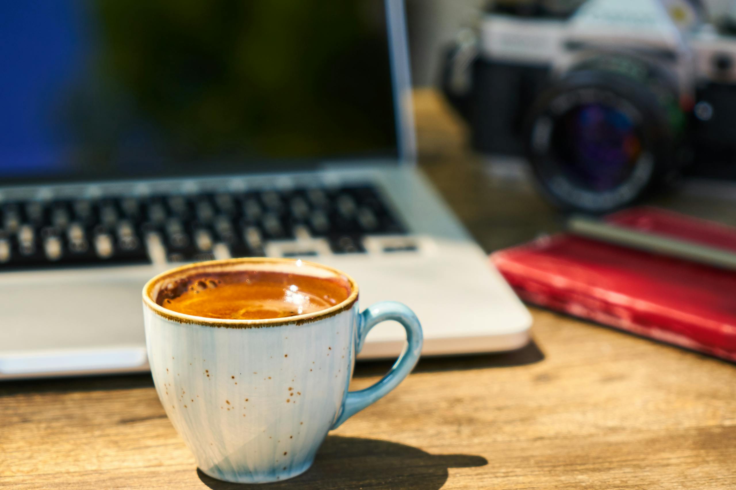 A cup of coffee and a laptop on a wooden table.