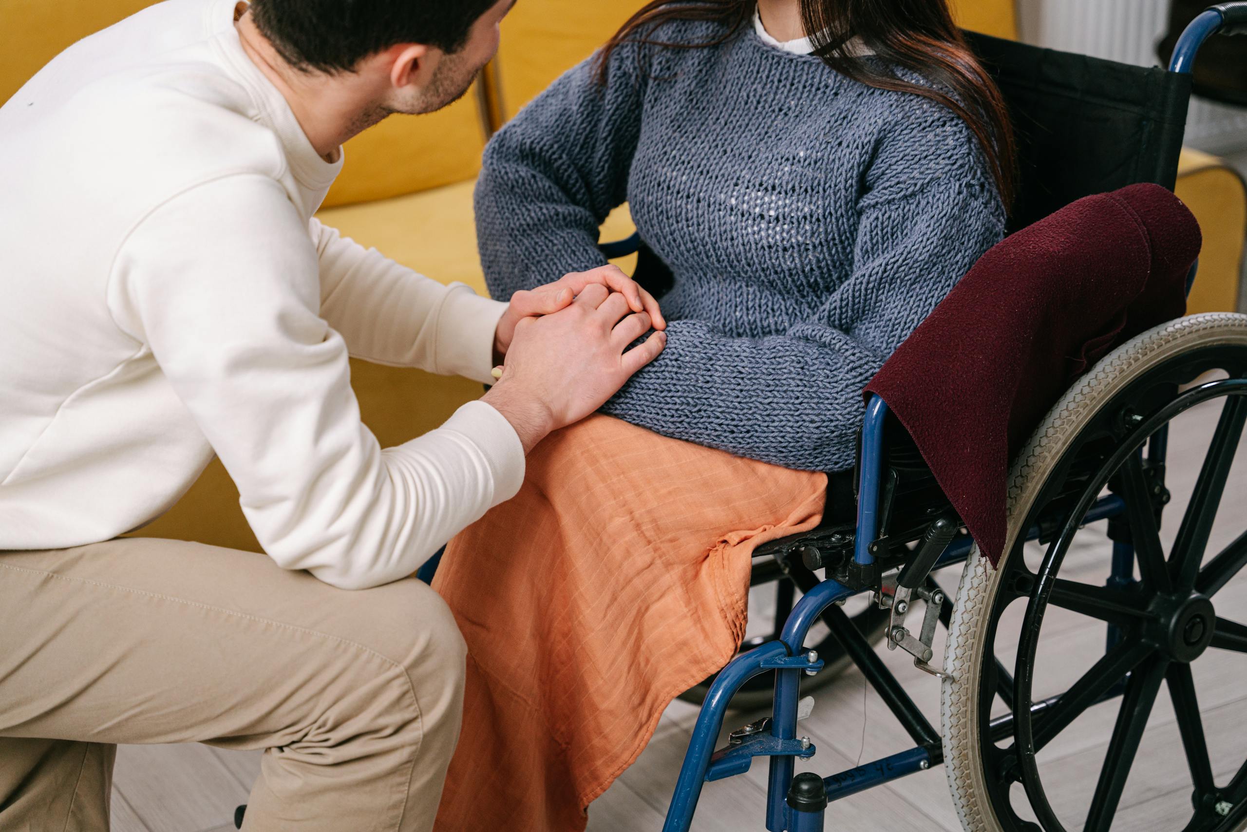 a middle-aged white man and woman hold hands. the woman is sitting in a wheelchair.