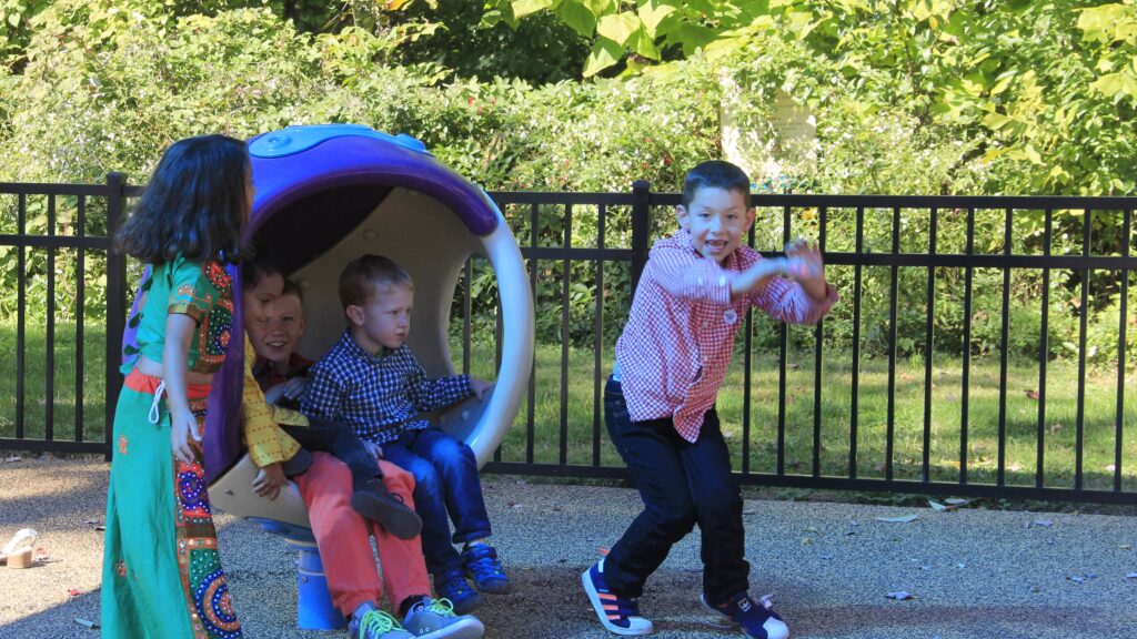 A male child dances in front of three children who sit in a circular structure.