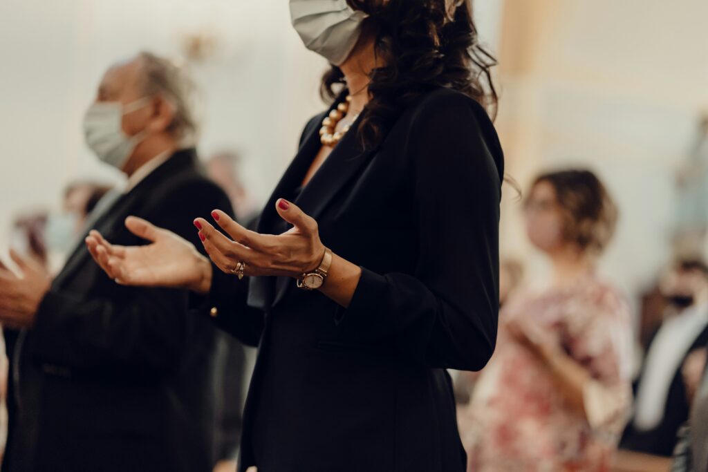 a woman wearing a mask raises her hands in worship