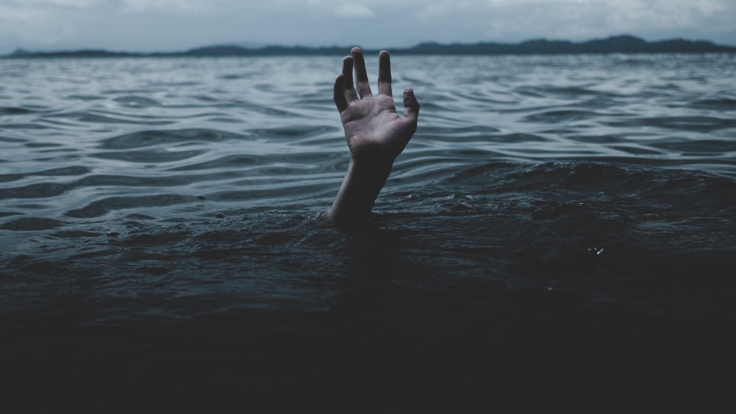 a human hand reaches up from a sea of water