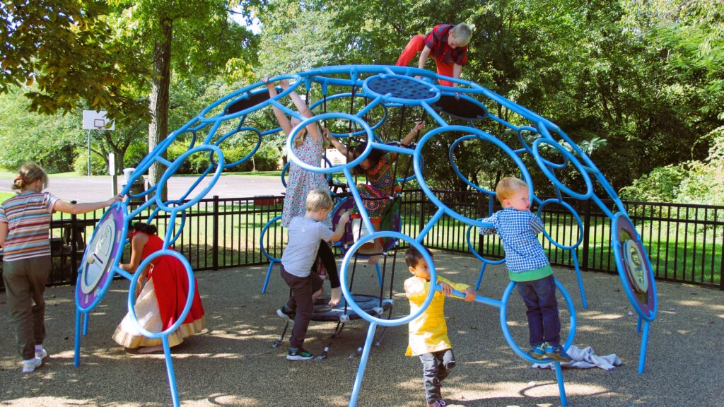 a group of children of various ethnicities and genders climb on a playground structure.