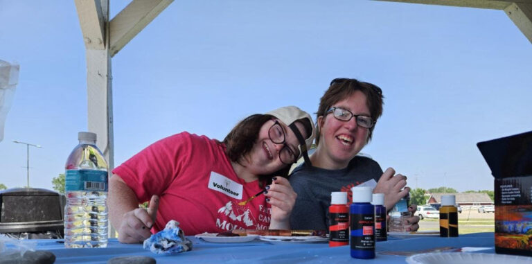 two white female young adults with signs of intellectual disabilities smile together.