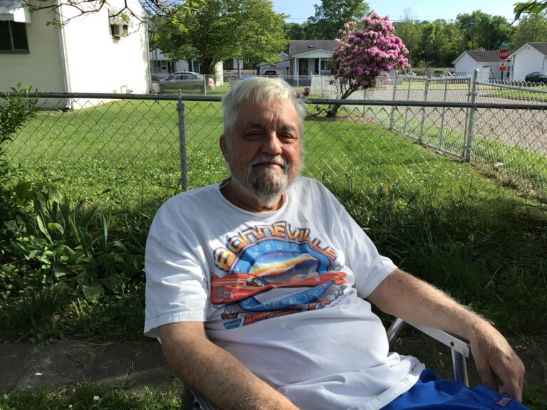 an elderly white man sits in a lawn chair in the summer.