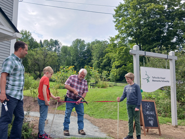 two preteens, one middle-aged man, and one older man ceremoniously cut a ribbon that stretches across a paved sidewalk.