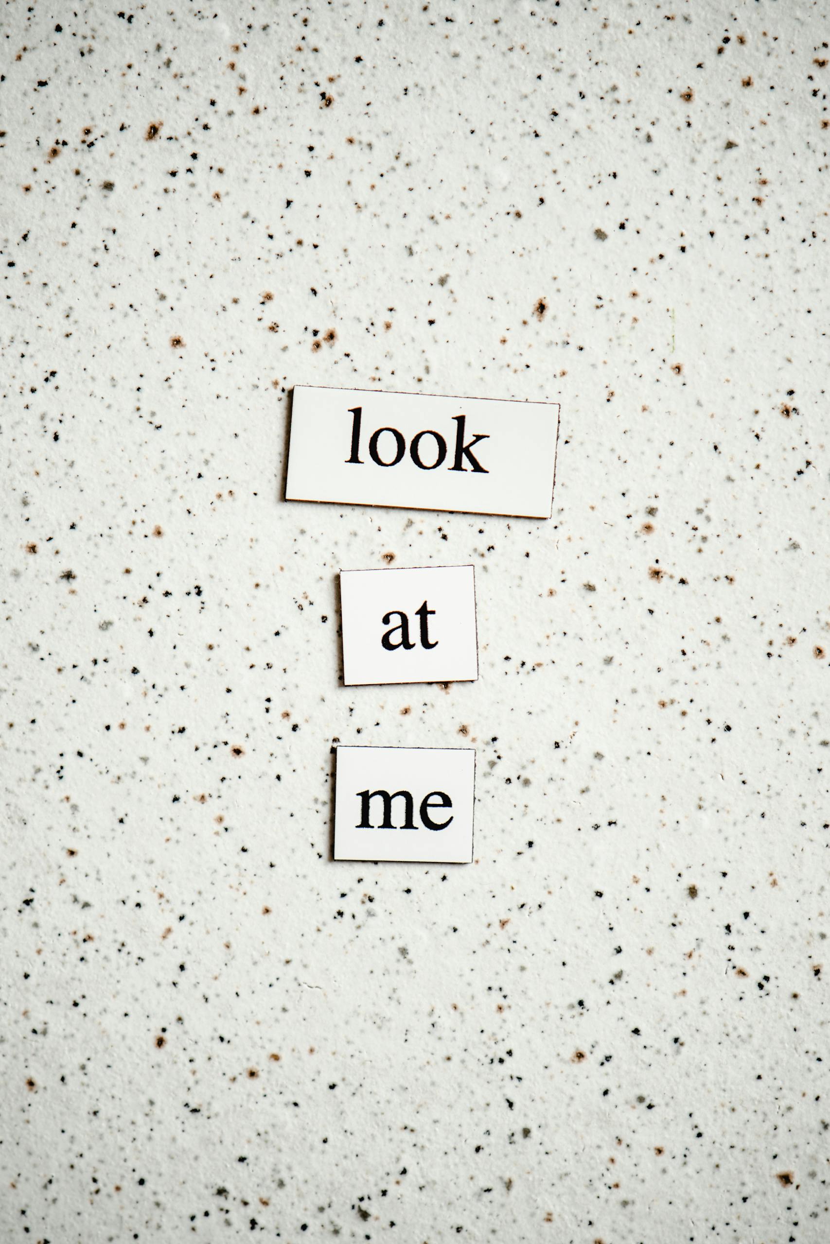 Minimalist text design with "look at me" on speckled surface.